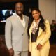 Full portrait of Nigerian entrepreneur Obi Cubana in a grey suit next to his wife Ebele Iyiegbu in a yellow double-breasted suit and silk scarf.