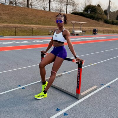 Nigerian world record holder Tobi Amusan sitting on a hurdle at a running track during a practice session.