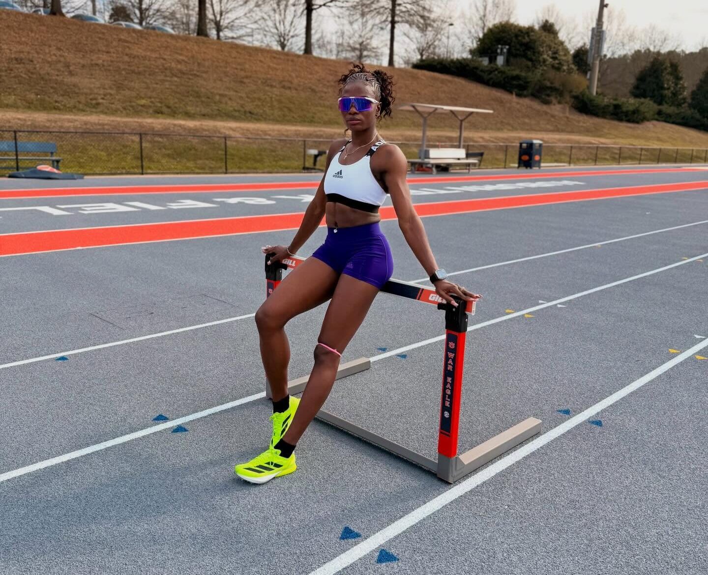 Nigerian world record holder Tobi Amusan sitting on a hurdle at a running track during a practice session.