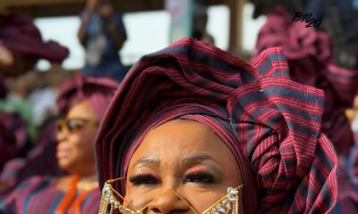 A woman at Ojude Oba 2026 wearing a frameless eyewear piece constructed entirely of gold chains and hanging crystals draped across her nose and cheeks.