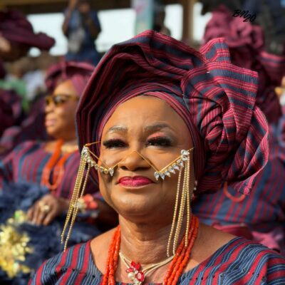 A woman at Ojude Oba 2026 wearing a frameless eyewear piece constructed entirely of gold chains and hanging crystals draped across her nose and cheeks.