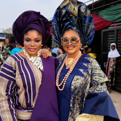 Nollywood actresses Eniola Ajao and Mercy Aigbe in traditional Yoruba Aso Oke and elaborate geles wearing statement sunglasses on the set of Iwe Ala.