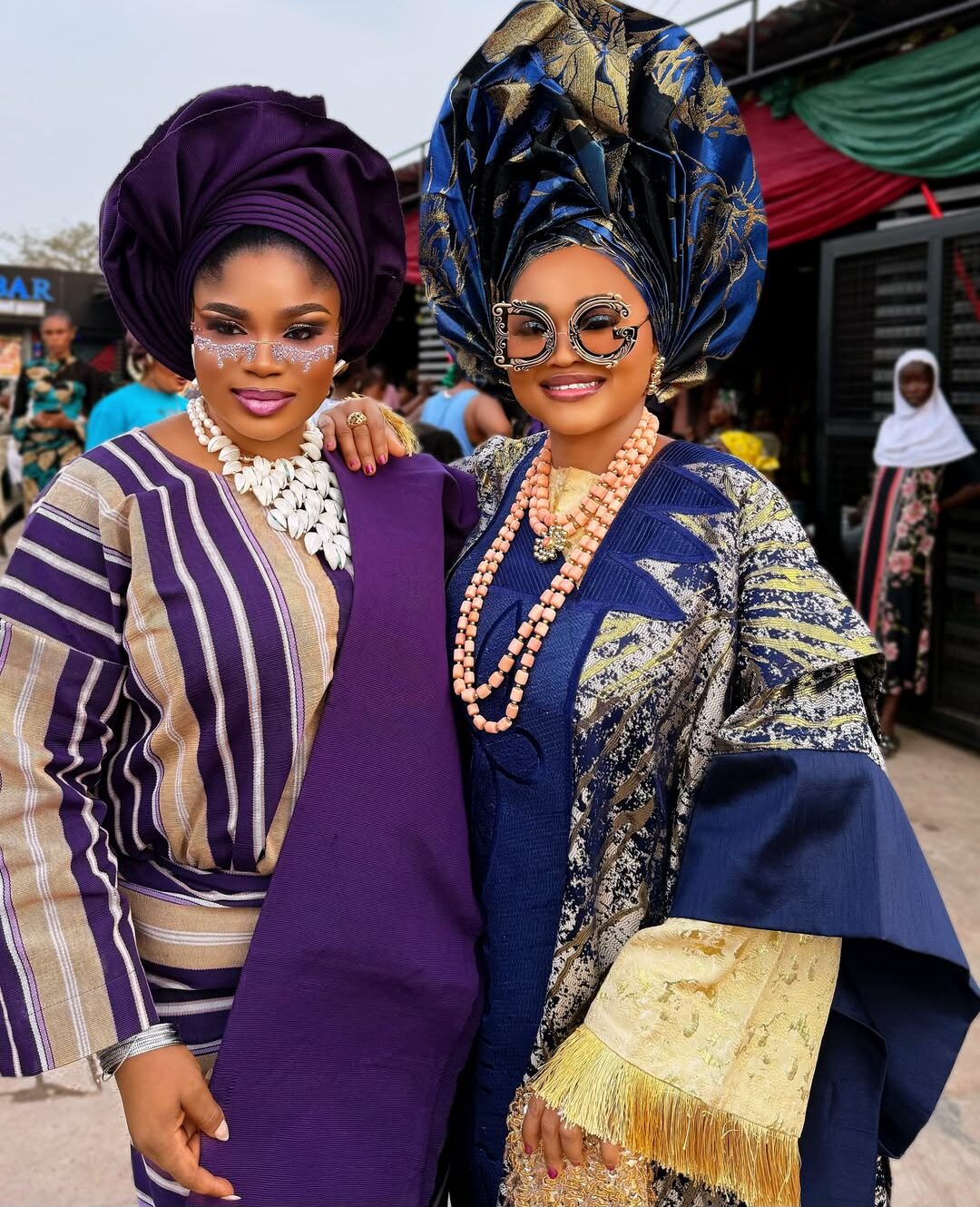 Nollywood actresses Eniola Ajao and Mercy Aigbe in traditional Yoruba Aso Oke and elaborate geles wearing statement sunglasses on the set of Iwe Ala.