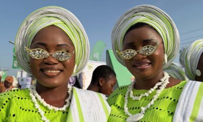 Two Ijebu-Ode women smiling at the Ojude Oba Festival wearing matching lime green buba, white and green gele, and stone-embellished sunglasses.