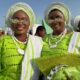 Two Ijebu-Ode women smiling at the Ojude Oba Festival wearing matching lime green buba, white and green gele, and stone-embellished sunglasses.
