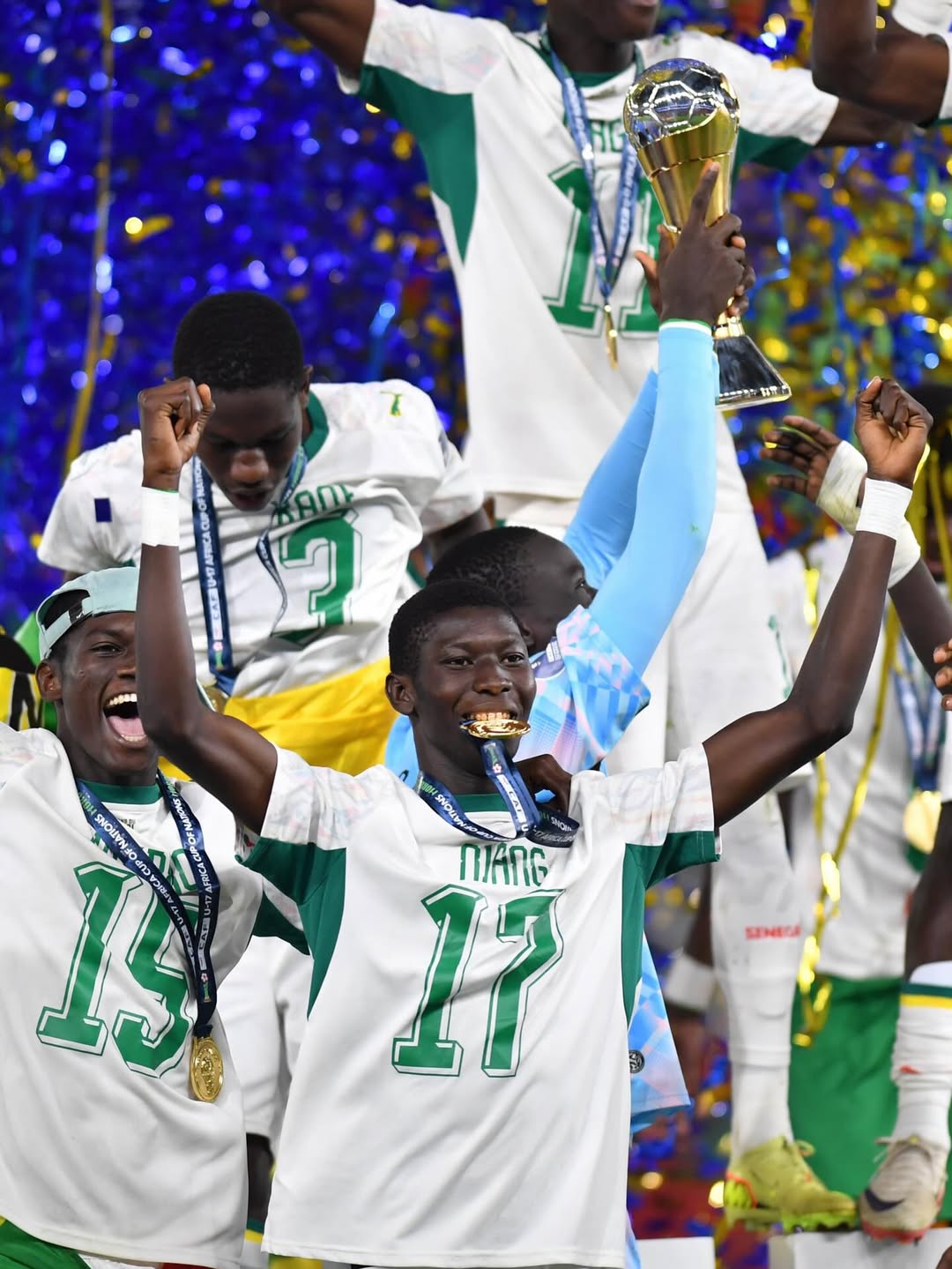 Close-up of joyous Senegal U17 football players, including number 17 Niang biting his gold medal, celebrating their AFCON final victory.