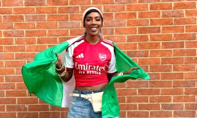 Afrobeats artist Tiwa Savage smiling while holding open the green and white Nigerian flag over her shoulders during the Arsenal trophy celebration in London.