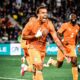 Ivory Coast forward Simon Adingra celebrating with teammates in their orange kit after scoring against France during a pre-World Cup 2026 friendly match.