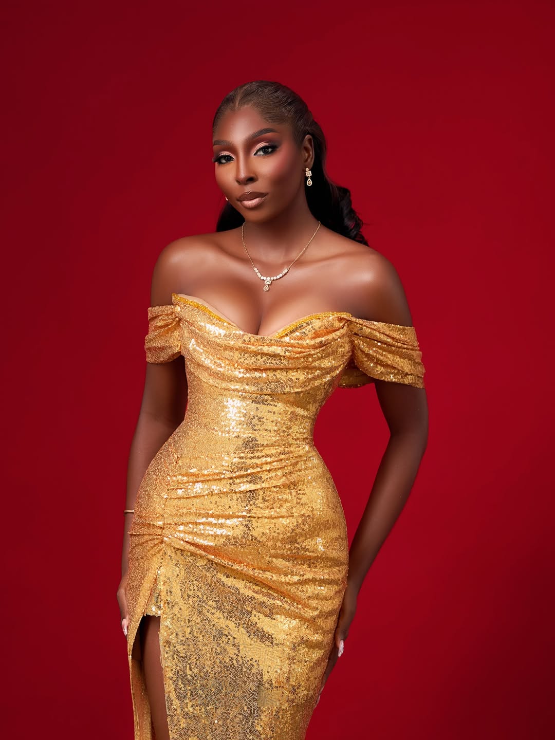 Miss World Nigeria 2026 Tamunosoye Karibi George wearing an off-the-shoulder gold sequined dress with a high slit against a red backdrop.