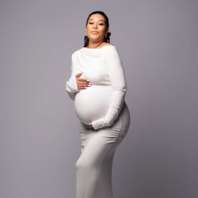 maternity shoot of Nollywood actress Adunni Ade wearing a form-fitting white long-sleeved dress and cradling her baby bump.