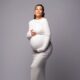 maternity shoot of Nollywood actress Adunni Ade wearing a form-fitting white long-sleeved dress and cradling her baby bump.