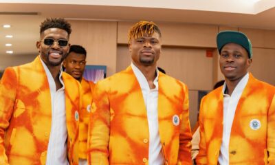 Côte d'Ivoire players Ibrahim Sangaré, Emmanuel Agbadou, and Wilfried Singo walking together with green and orange luxury travel luggage in their formal team suits.