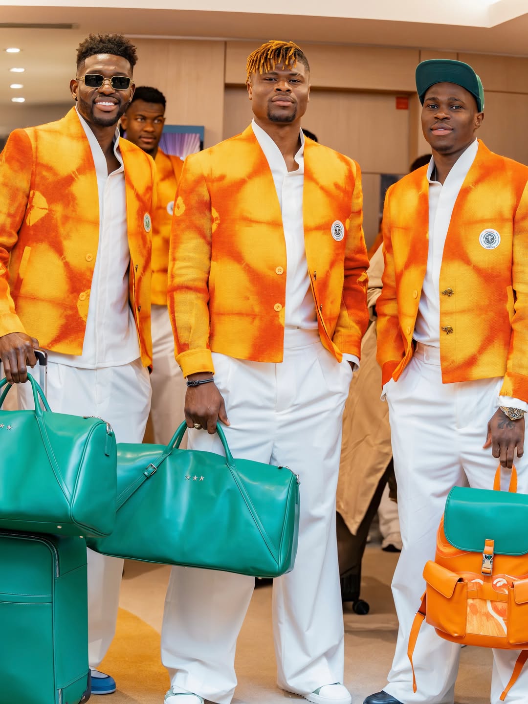 Côte d'Ivoire players Ibrahim Sangaré, Emmanuel Agbadou, and Wilfried Singo walking together with green and orange luxury travel luggage in their formal team suits.