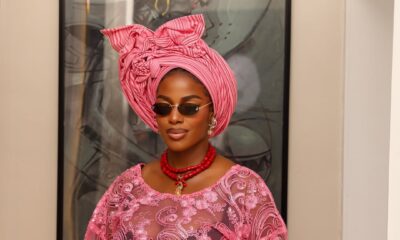 Portrait of Hilda Baci highlighting her sheer pink floral lace buba bodice, chunky red coral bead necklace, and retro sunglasses, styled by Emmanuel Goodnews.
