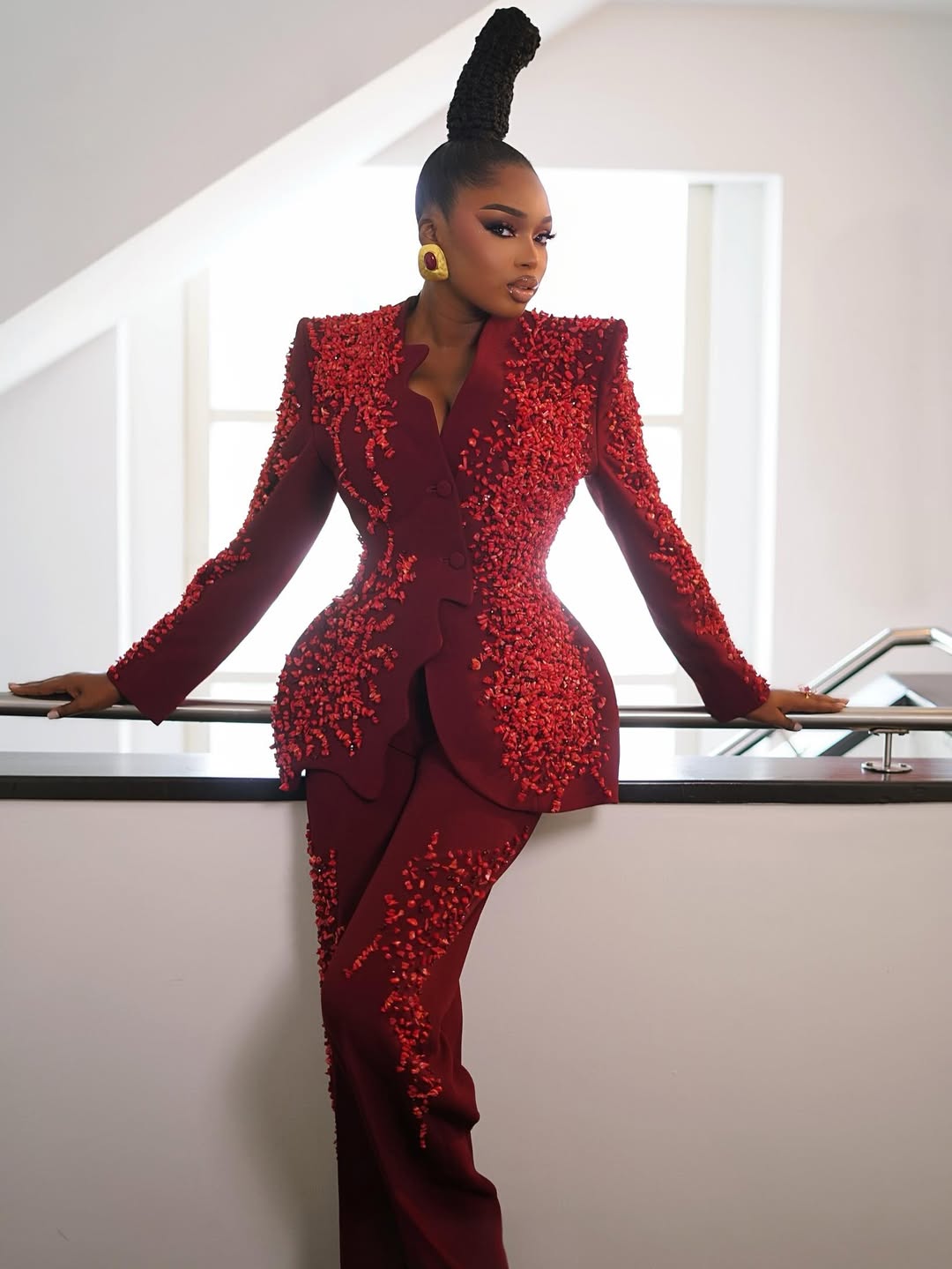 Sabrina Idukpaye in a burgundy trousersuit with a sculpted hourglass silhouette and red stone details.