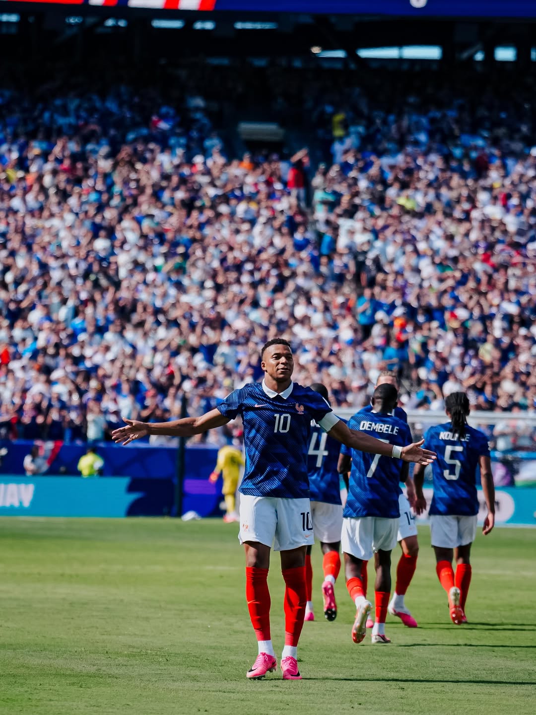 Kylian Mbappe standing with open arms facing the stadium crowd after France's win over Senegal.