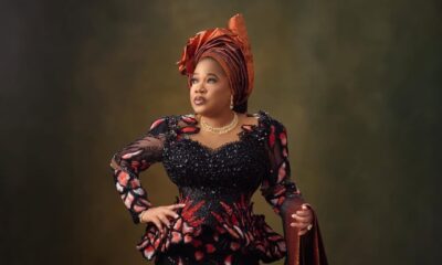 Toyin Abraham Ajeyemi posing with one hand on her hip, wearing a pleated copper architectural gele, a terracotta beaded lace outfit, and holding a matching ipele over her arm.