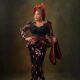 Toyin Abraham Ajeyemi posing with one hand on her hip, wearing a pleated copper architectural gele, a terracotta beaded lace outfit, and holding a matching ipele over her arm.