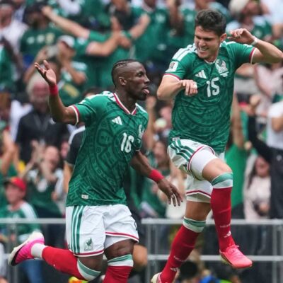 Julián Quiñones running and celebrating the opening goal for Mexico on the pitch at Estadio Azteca.