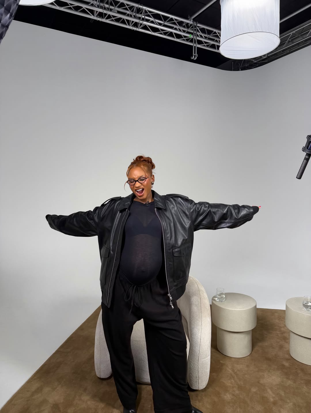 Temi Otedola poses with open arms wearing an oversized black leather jacket over a black maternity outfit.
