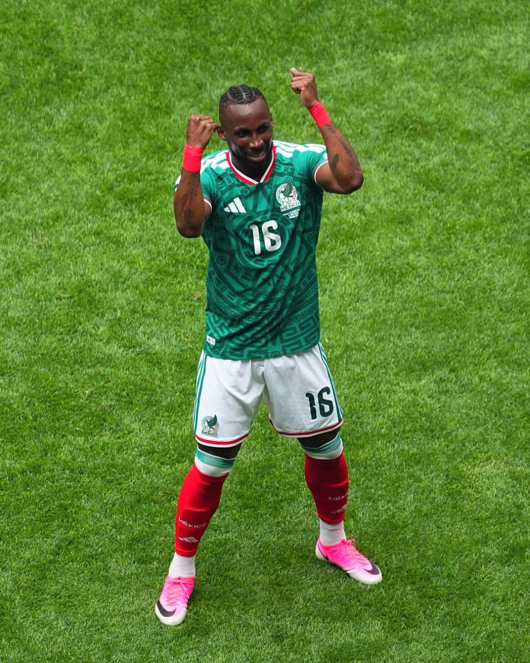 Julián Quiñones standing on the grass with clenched fists celebrating his goal for Mexico.