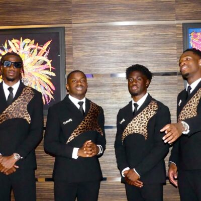 Four DR Congo players standing indoors in matching black-tie suits with leopard details and dark sunglasses.