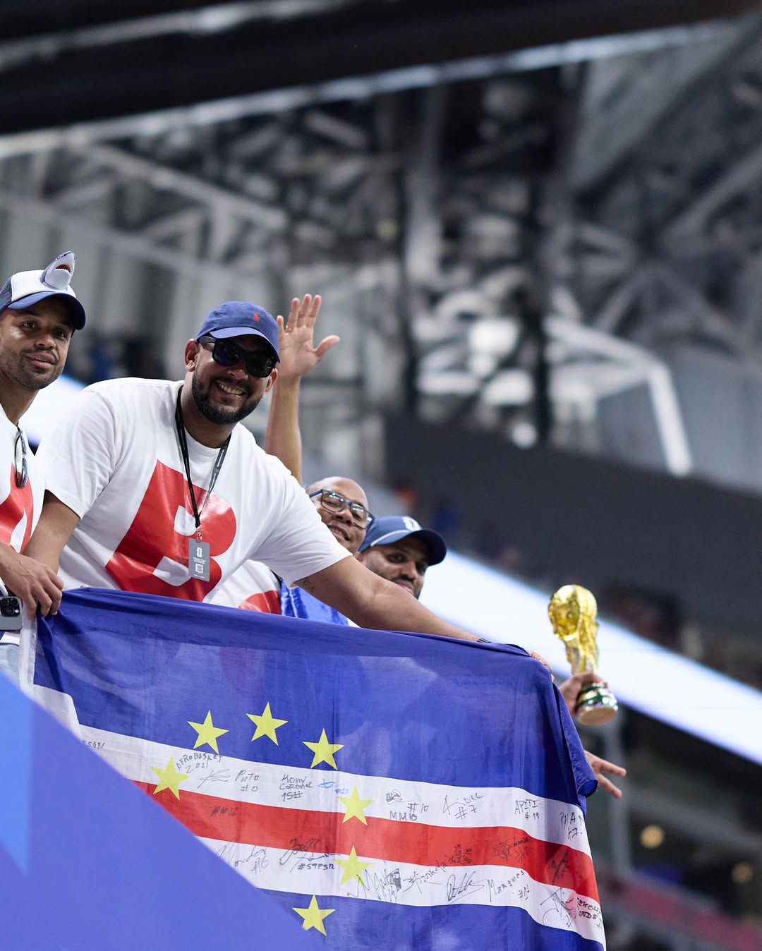 Cabo Verde football fans smiling and waving while holding a signed national flag in the stadium stands during the FIFA World Cup 2026.