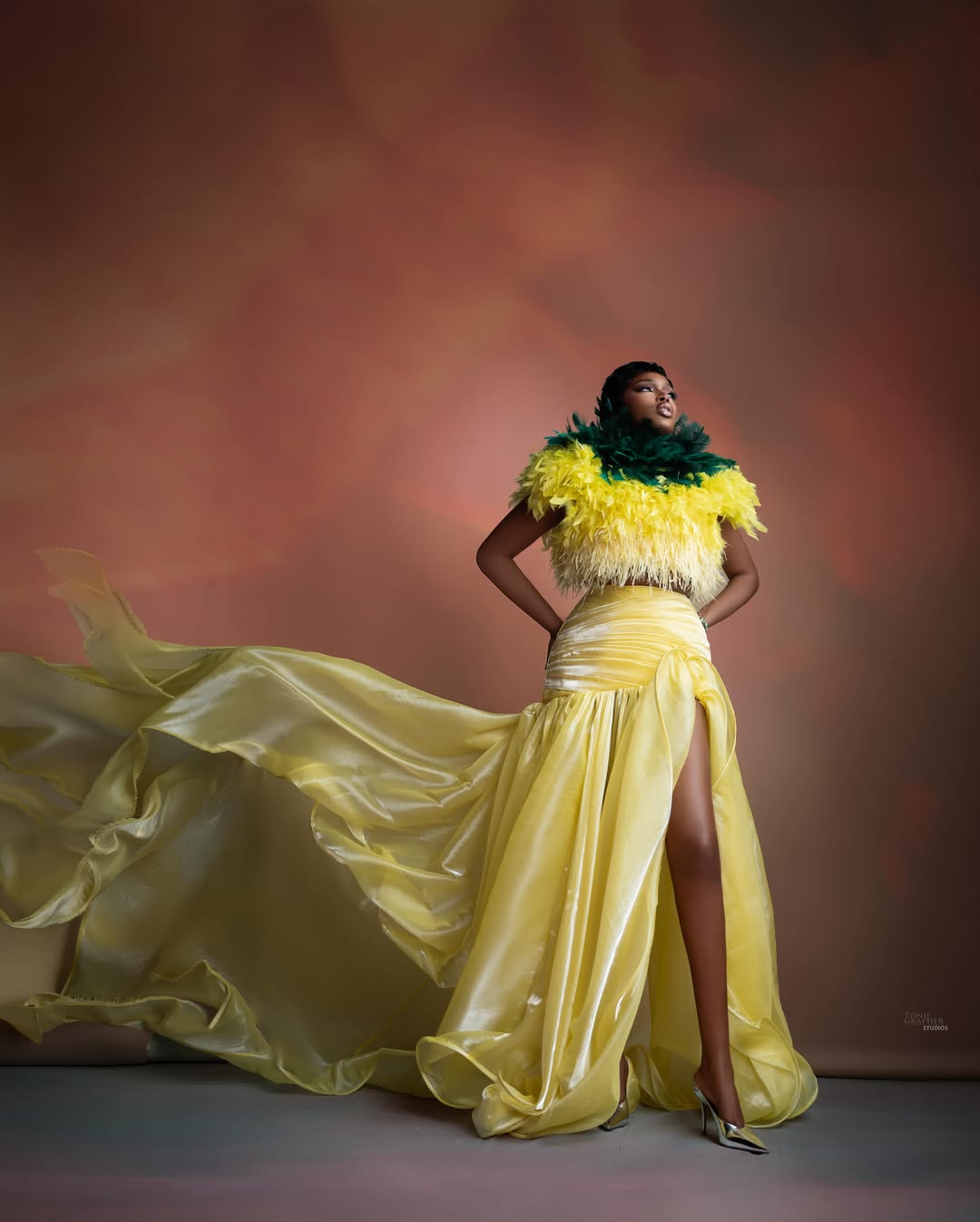 Sabrina Idukpaye in a bright yellow and forest green feathered bodice with a flowing yellow skirt and silver heels.