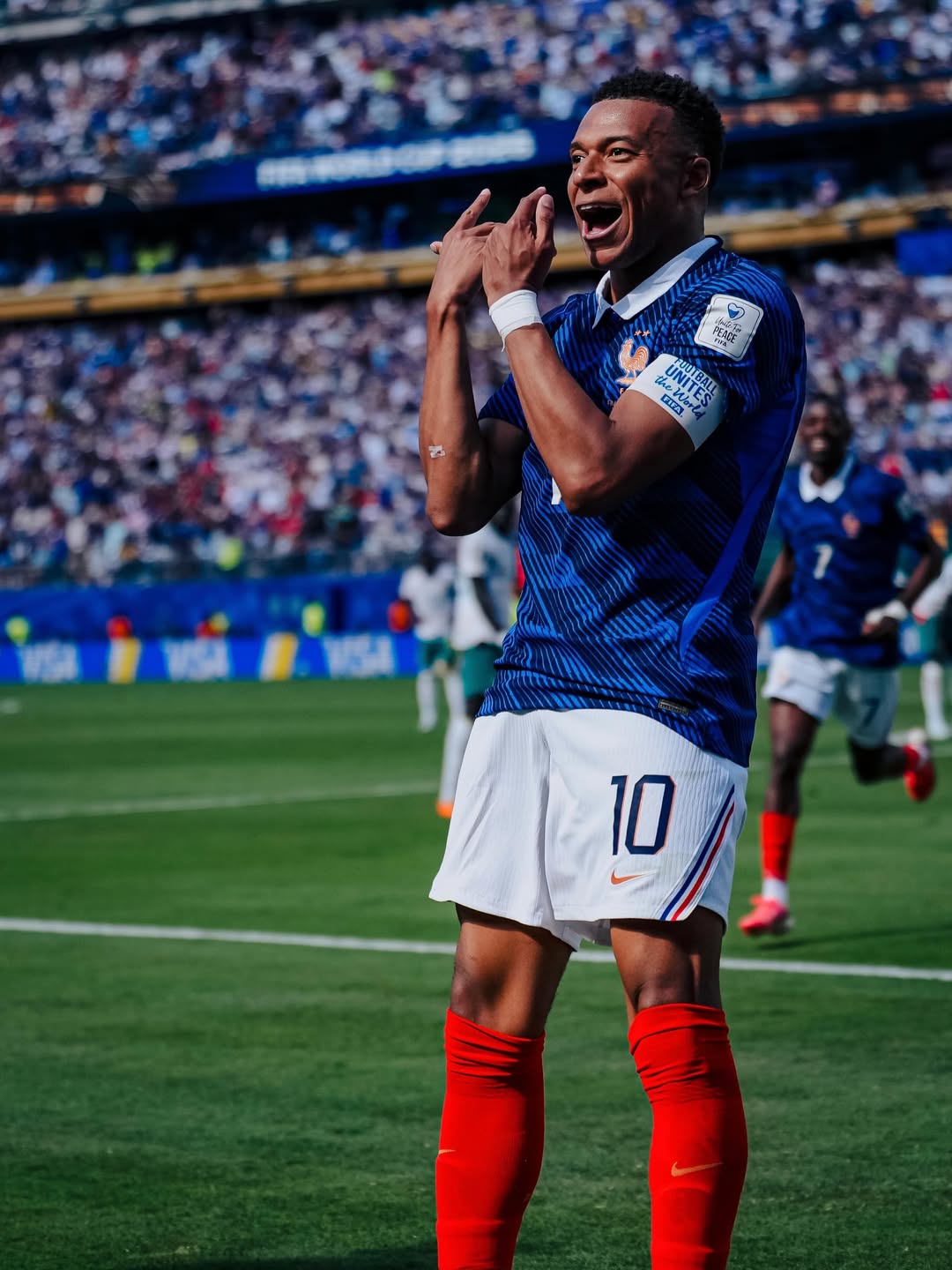 Kylian Mbappe shouting in celebration with his hands raised on the pitch after scoring for France against Senegal.