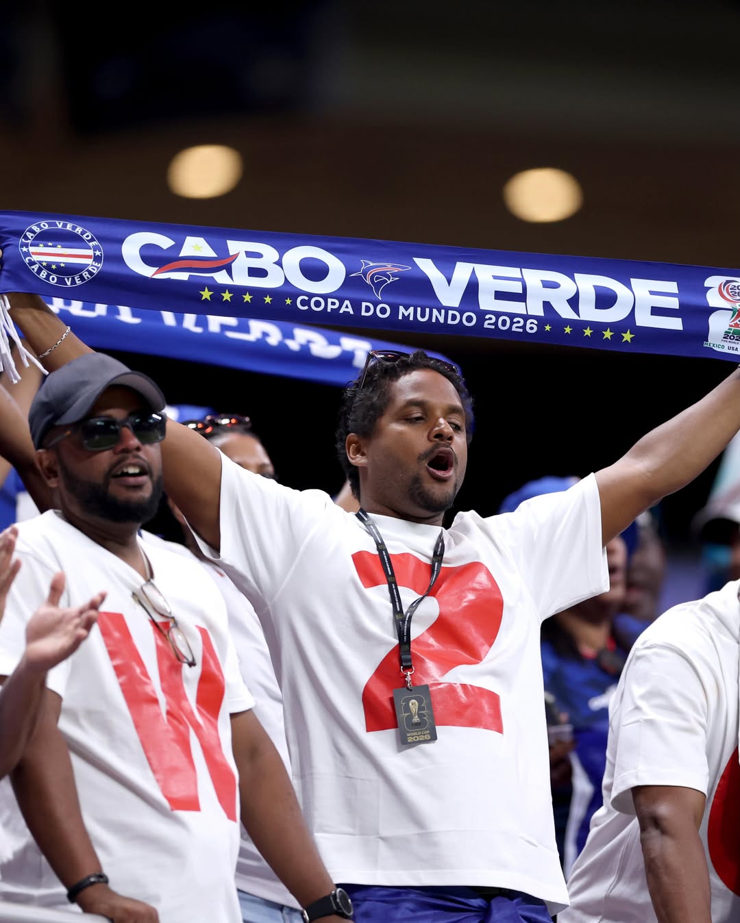 Passionate Cabo Verde football fans chanting in the stadium while holding up an official tournament scarf that reads Copa Do Mundo 2026.