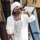 Rema holds a microphone to his mouth while wearing a white hooded jacket, a matched white wrap, and his angel chain pendant.
