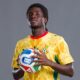 Studio portrait of Ghana national team football player Caleb Marfo Yirenkyi holding a FIFA match ball while wearing the official yellow and green patterned kit.