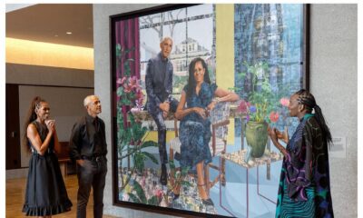 Barack and Michelle Obama stand in a gallery looking at their large-scale joint portrait while Nigerian artist Njideka Akunyili Crosby gestures and speaks.