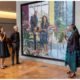Barack and Michelle Obama stand in a gallery looking at their large-scale joint portrait while Nigerian artist Njideka Akunyili Crosby gestures and speaks.
