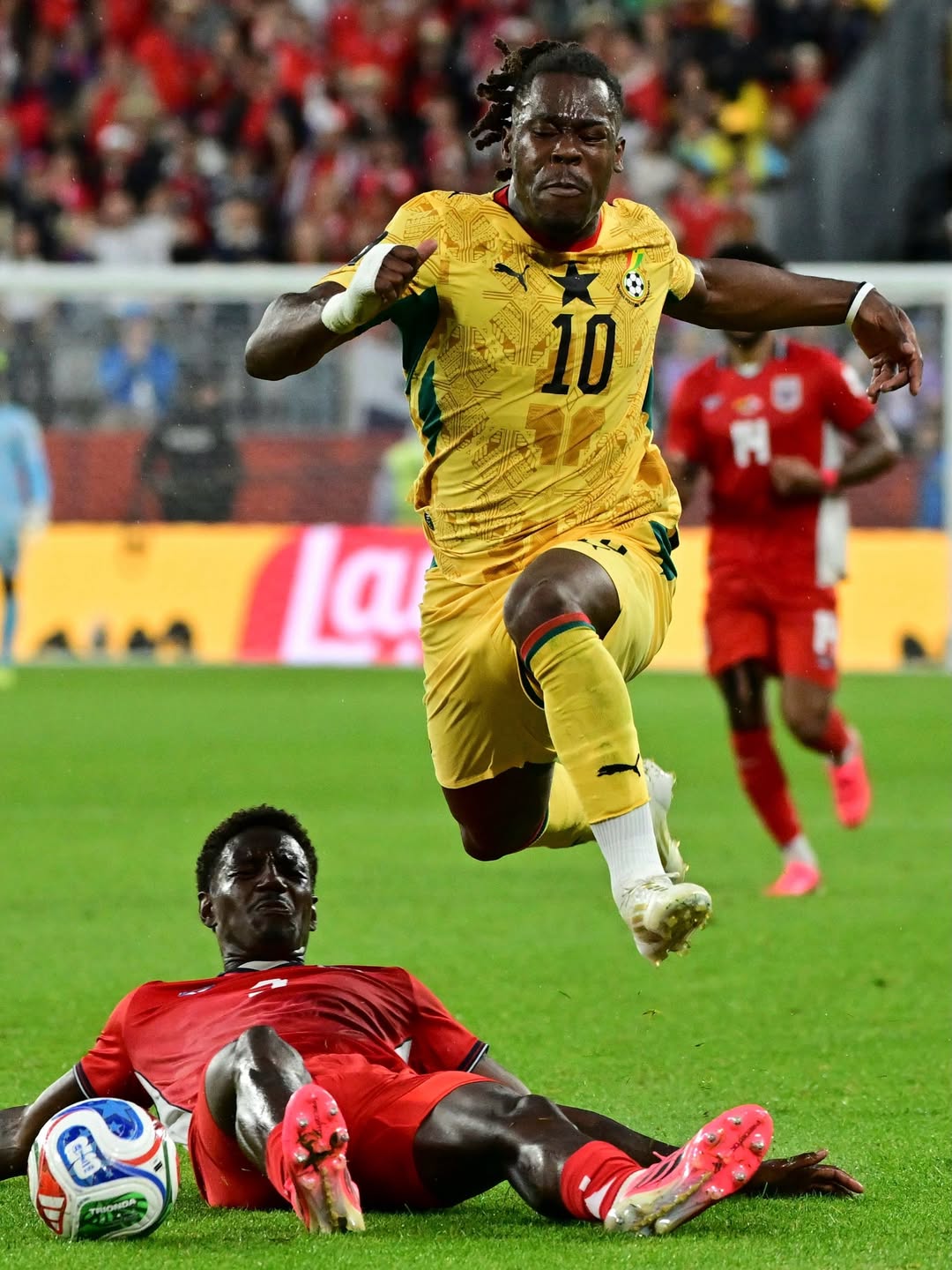 Ghana forward Brandon Thomas-Asante wearing the yellow number 10 jersey leaping past a sliding Panamanian defender during the 2026 FIFA World Cup group match in Toronto.