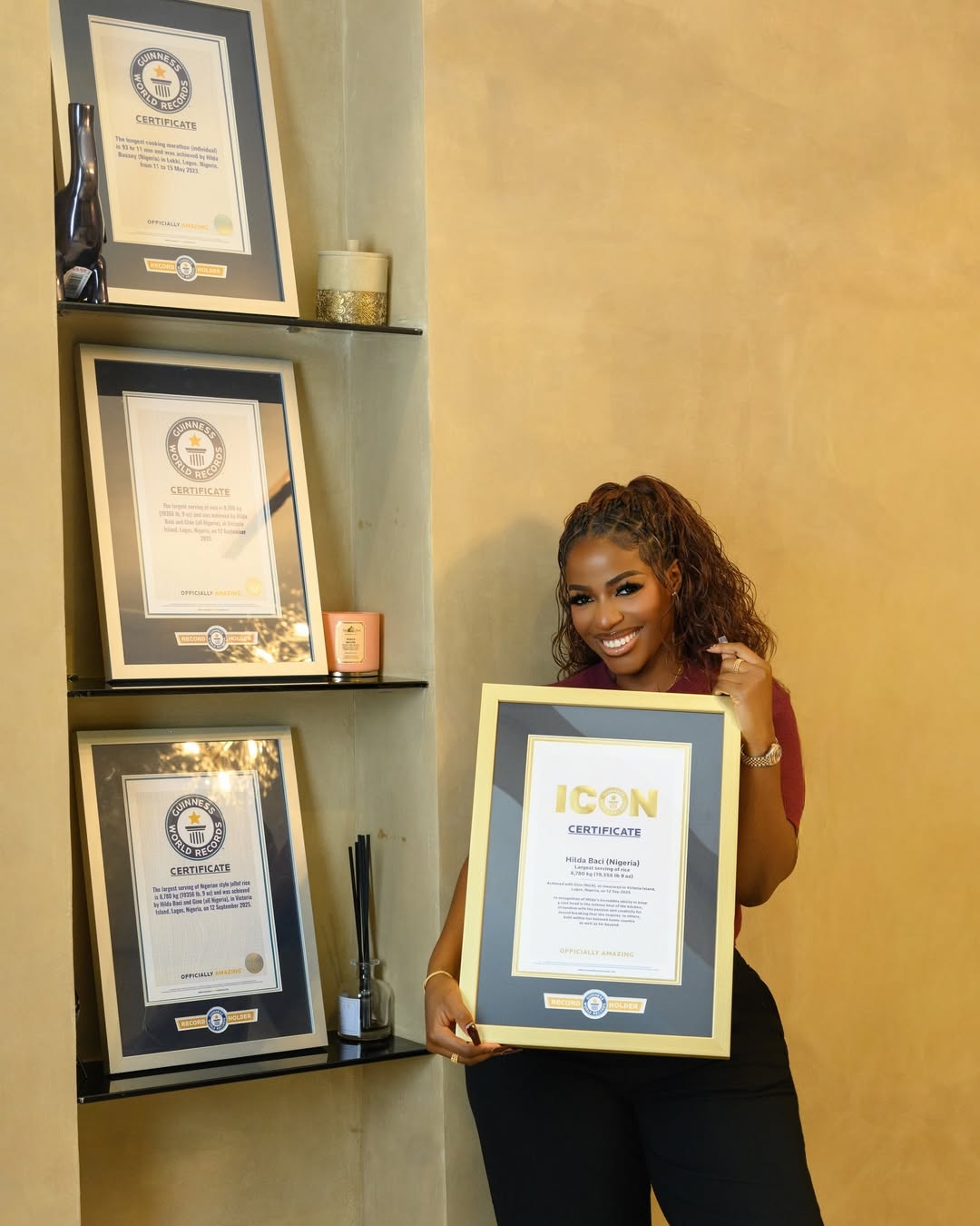 Triple world record holder Hilda Baci smiling while holding her framed Guinness World Records Icon certificate in front of a shelf displaying her other official plaques.