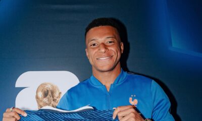 Kylian Mbappe proudly holding up a blue France football jersey printed with his name and the record number 58.