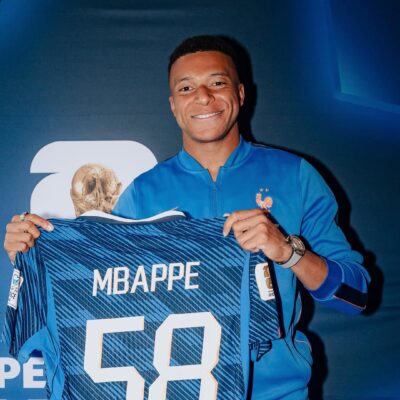 Kylian Mbappe proudly holding up a blue France football jersey printed with his name and the record number 58.
