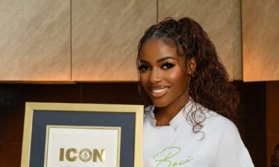 A portrait of Nigerian culinary star Hilda Baci in a white chef top presenting her official framed Guinness World Records Icon certificate.
