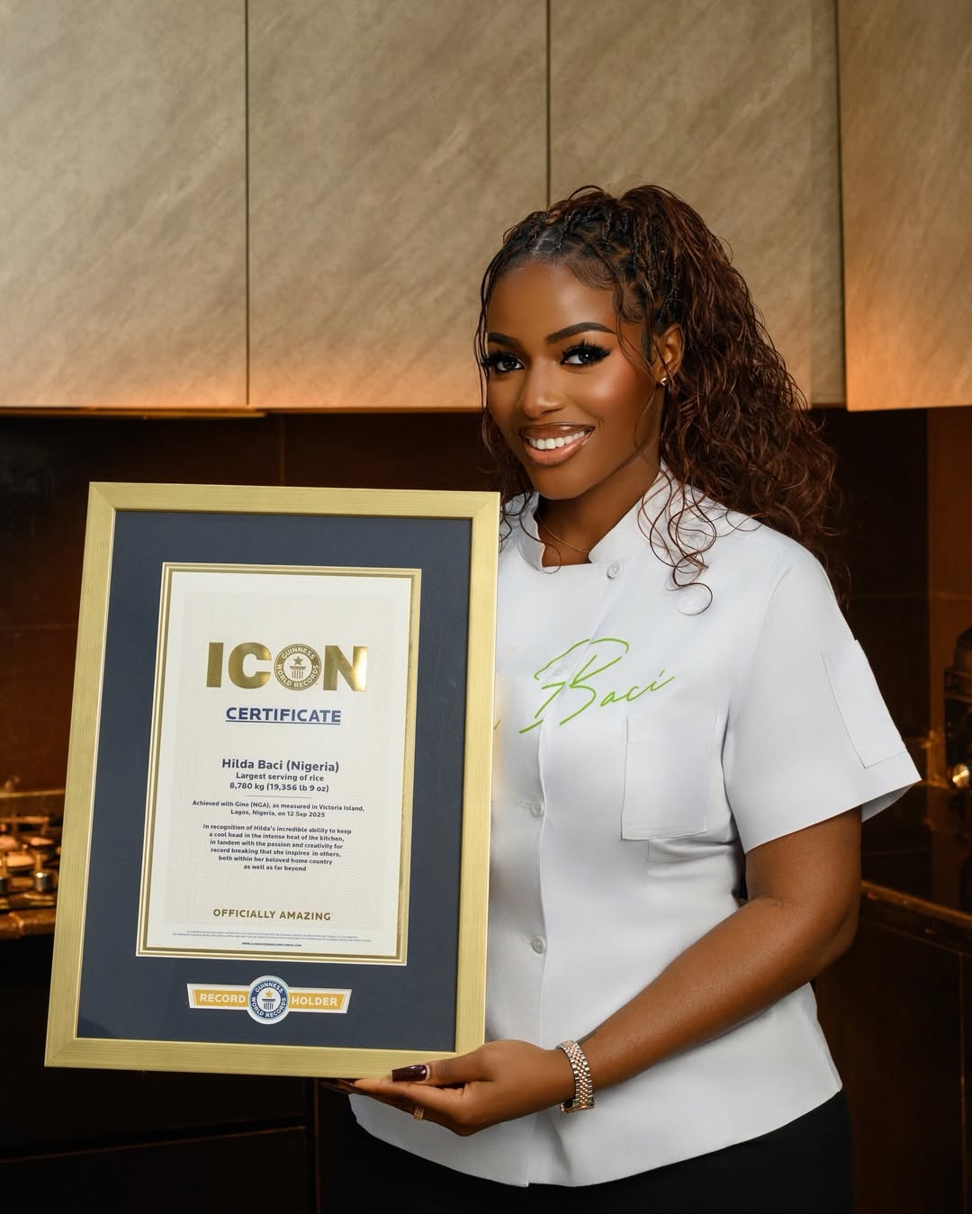 A portrait of Nigerian culinary star Hilda Baci in a white chef top presenting her official framed Guinness World Records Icon certificate.