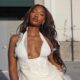 Tems wearing an ivory cream halter dress with a plunging mesh neckline, textured embroidery, beadwork, and soft white feather accents.
