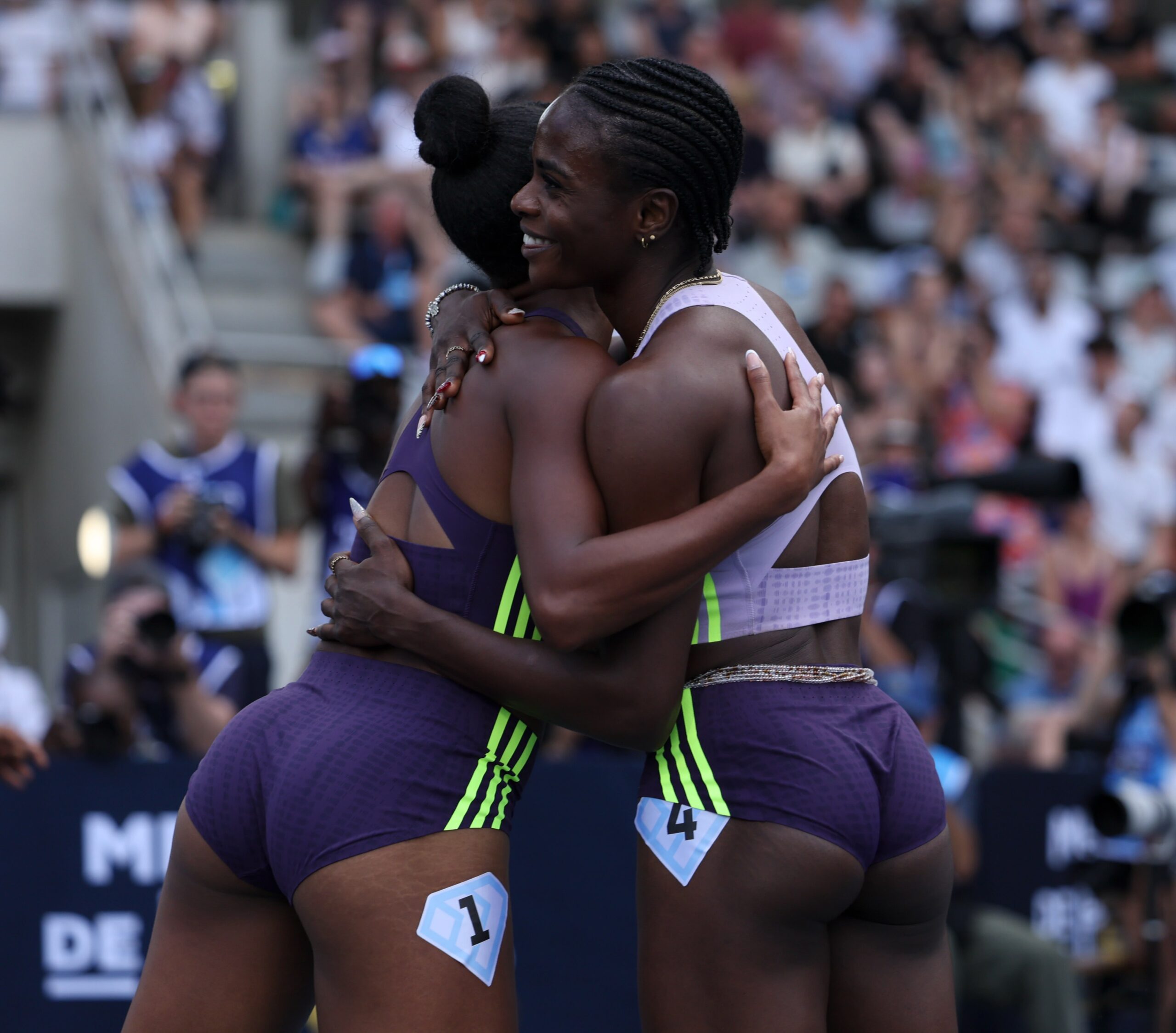Tobi Amusan smiling and embracing a fellow athlete on the track after winning the 100m hurdles race in France.