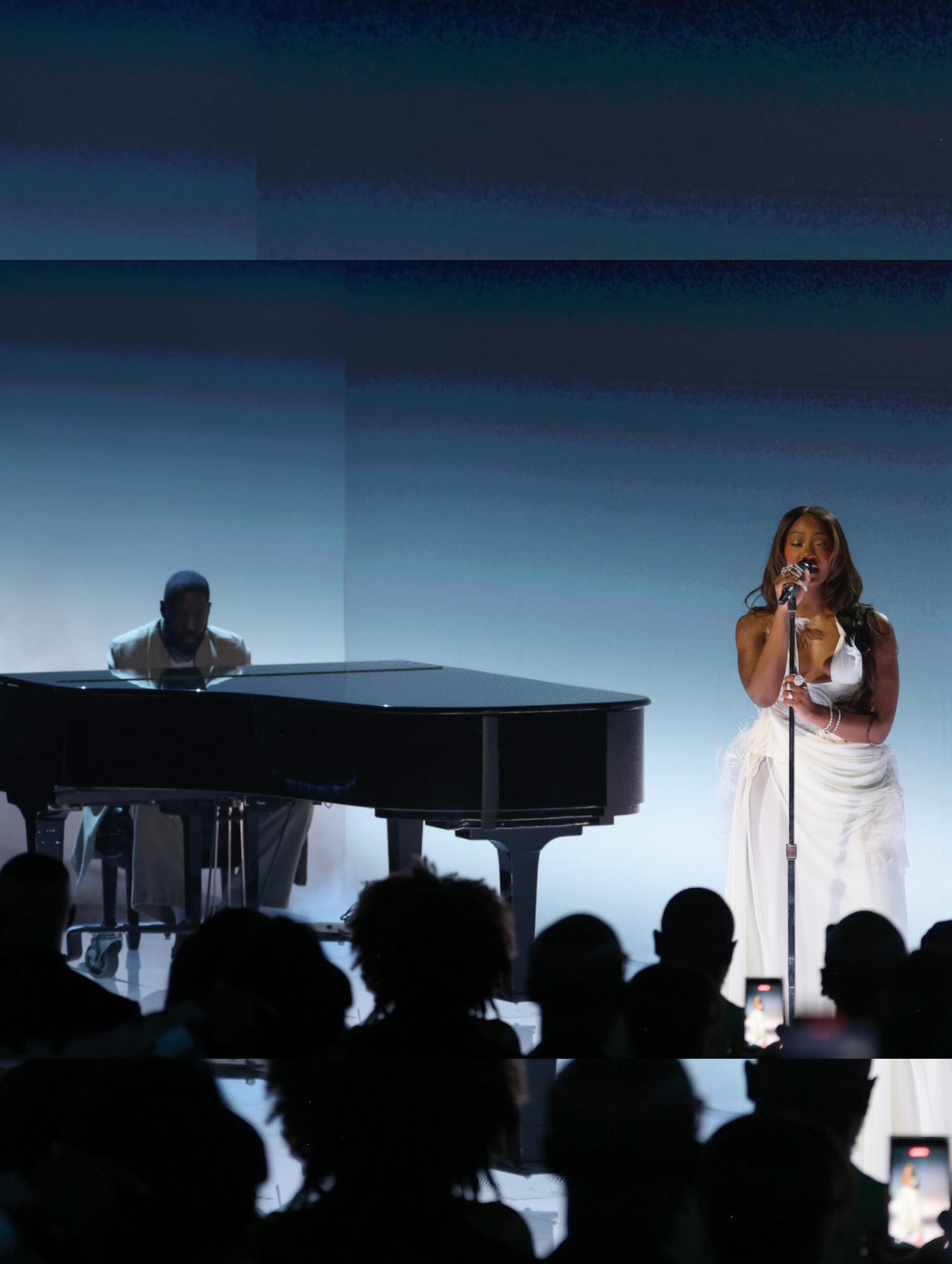 Tems singing into a microphone on stage at the 2026 BET Awards in an ivory dress, accompanied by a musician playing a black grand piano.