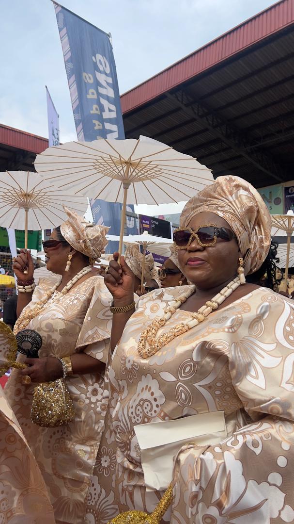 Ijebu-Ode women holding white paper parasols while dressed in cream and gold patterned damask buba and iro with matching geles.