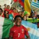 IShowSpeed wearing a red Portugal jersey with number 7, shouting excitedly in a stadium surrounded by diverse football fans holding flags from Nigeria, Argentina, Brazil, and Uruguay.