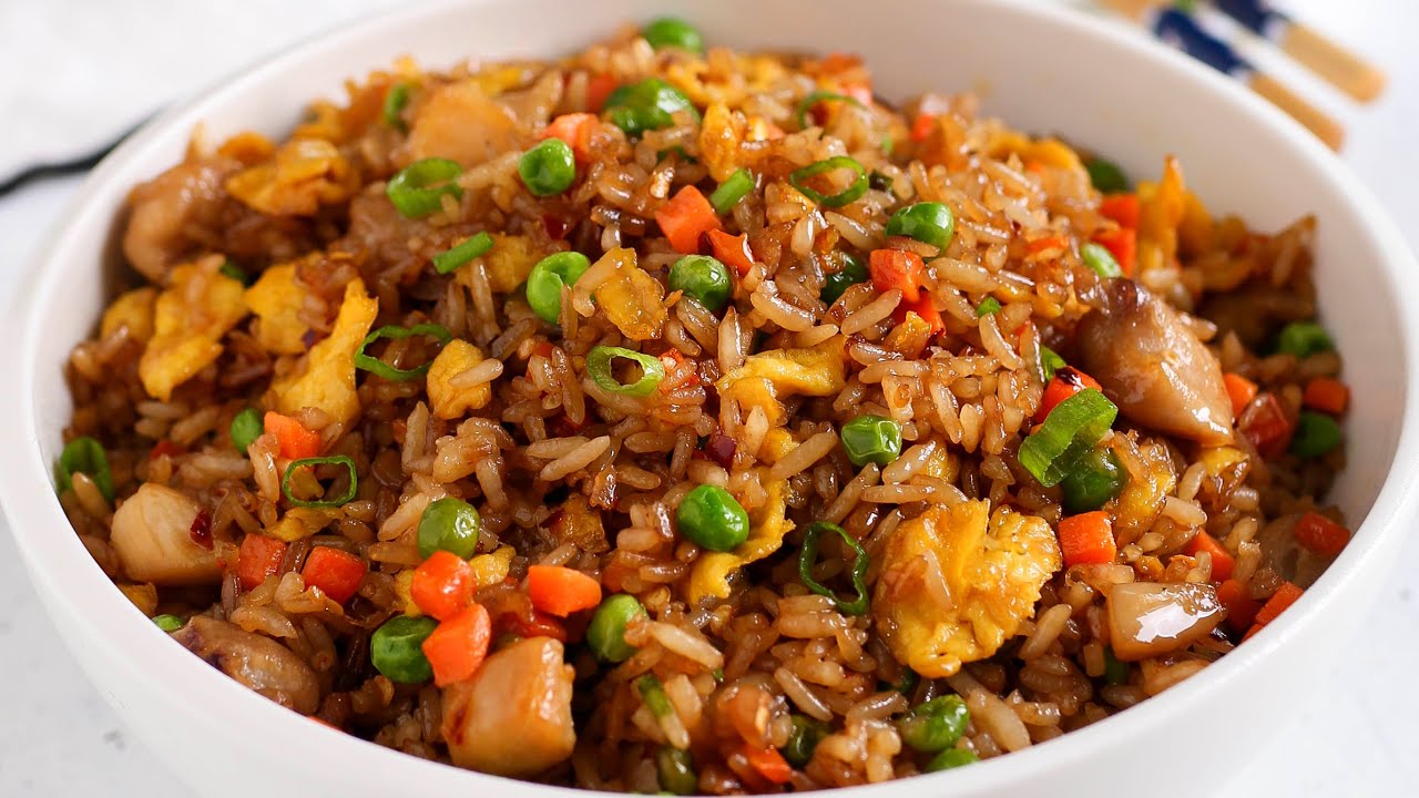 A white bowl filled with authentic Chinese chicken fried rice by Kikifoodies, showing fluffy, separate grains of day-old rice mixed with scrambled eggs, green peas, diced carrots, and chopped scallions.