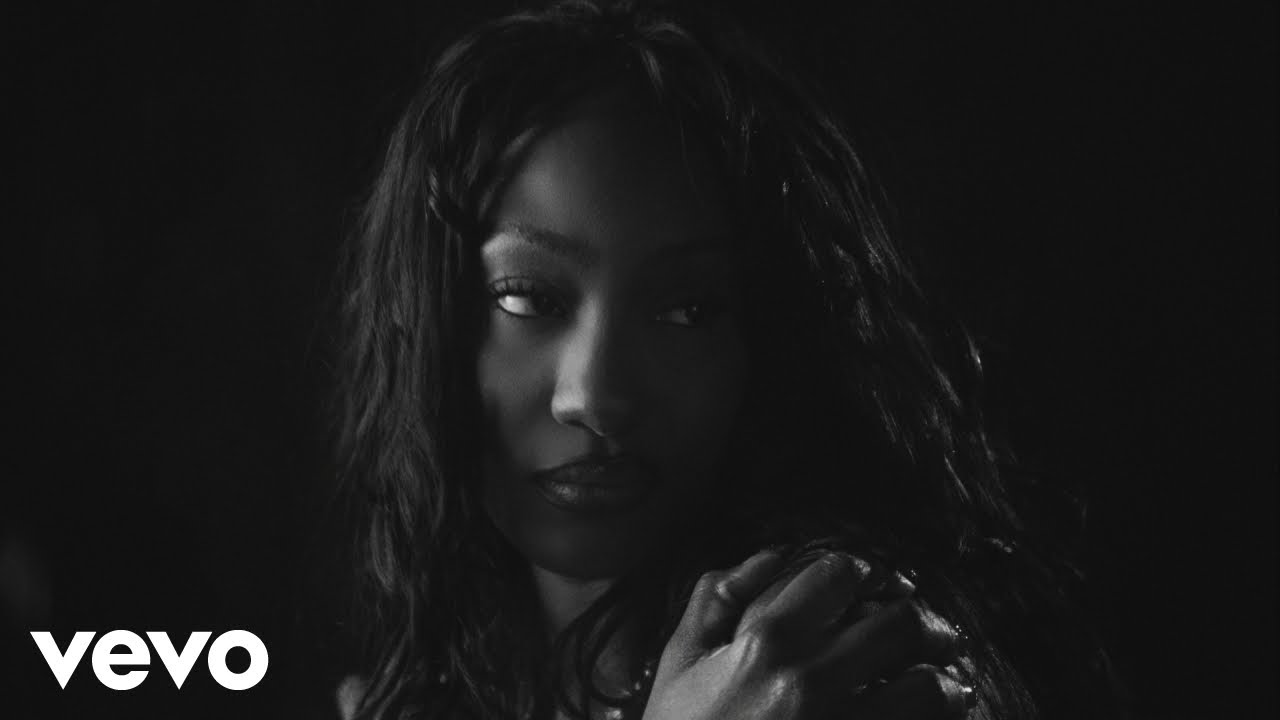 A close-up black and white music video still of Tems looking to the side against a dark background with a Vevo logo in the bottom left corner.