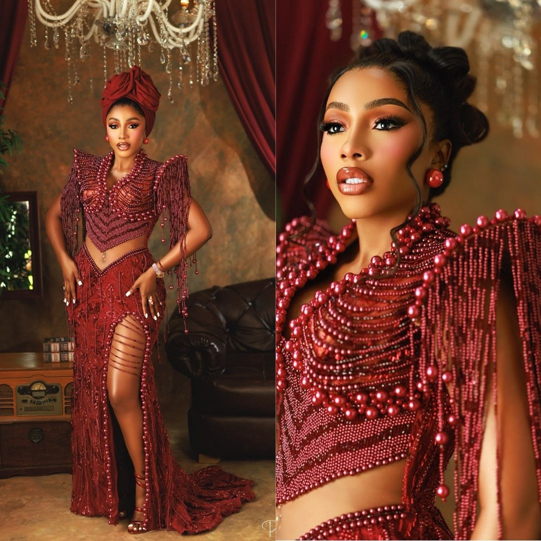 Mercy Eke wearing a crimson corset two-piece look featuring heavy pearl fringe draping, high thigh split, and a matching folded gele headpiece.