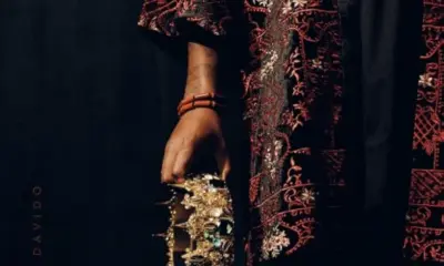 Official album cover art for Oriade by Davido featuring a close-up profile of an embroidered traditional garment and a hand holding a detailed gold crown adorned with green gemstones against a dark background.