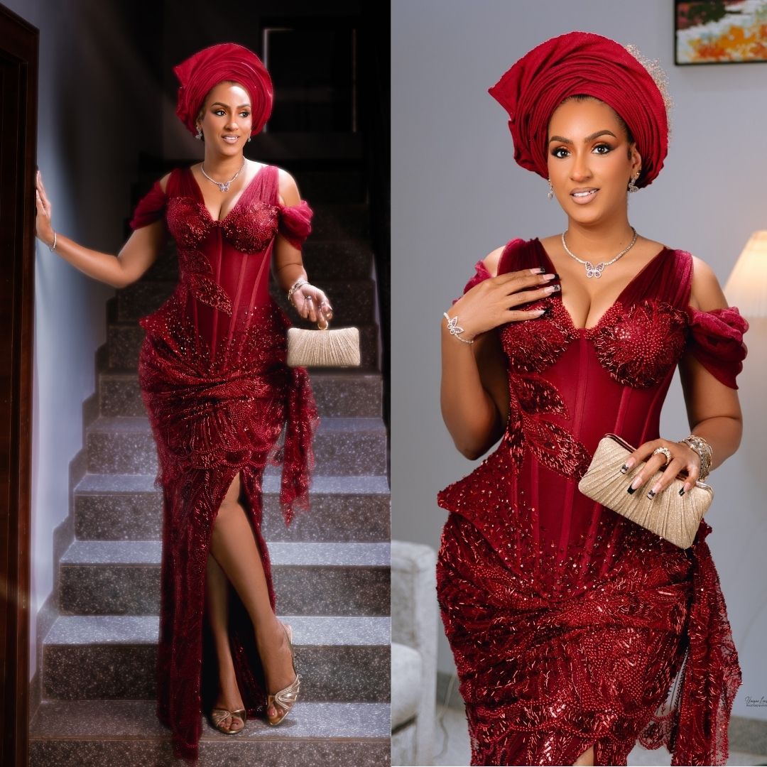 Juliet Ibrahim wearing a cold-shoulder wine-red net lace gown with sheer corset boning, draped thigh split, folded gele, and metallic gold clutch.